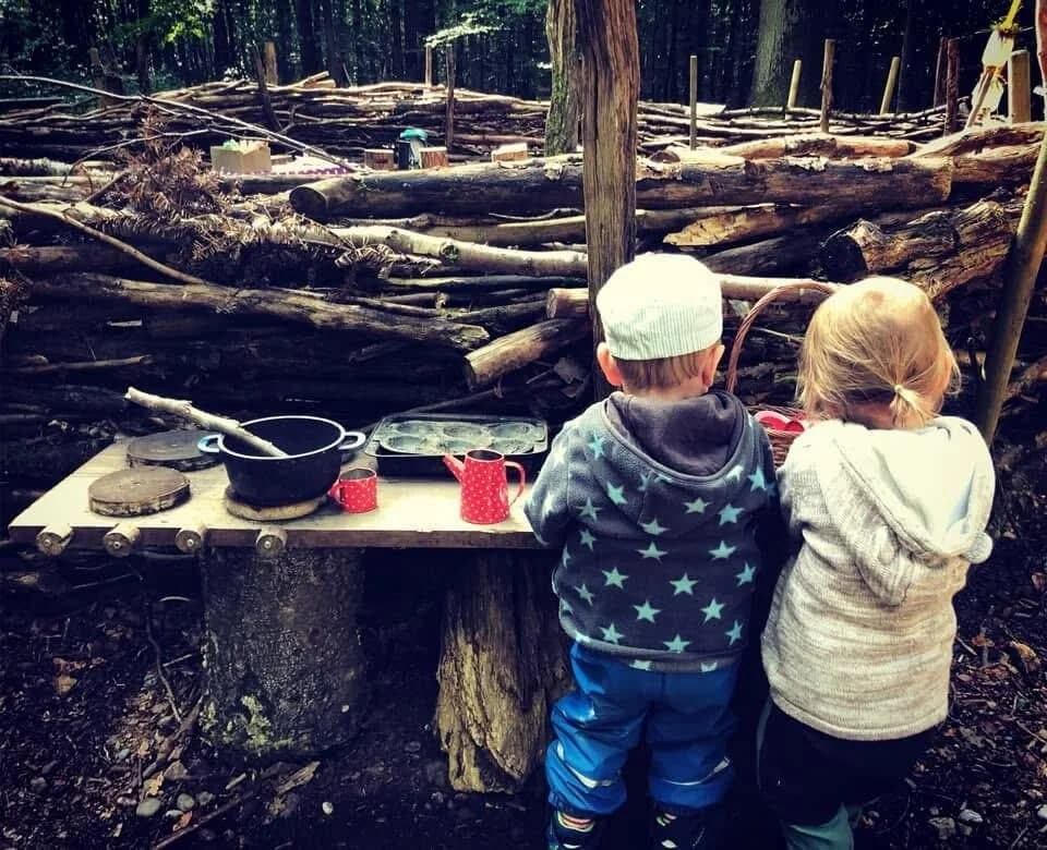 Zwei Kinder spielen gemeinsam an einer Waldküche