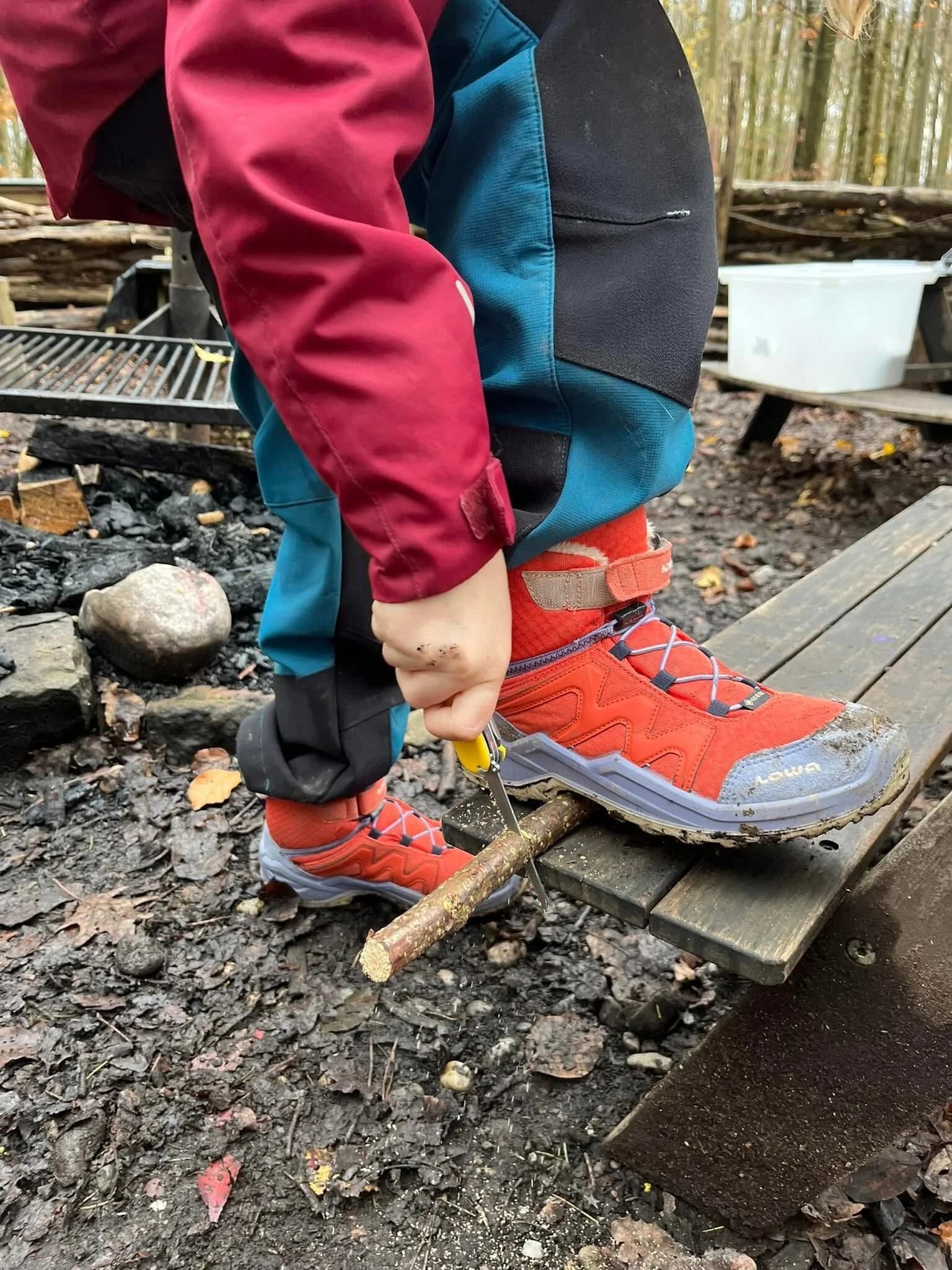 Kind schnitzt mit einem Taschenmesser einen Ast