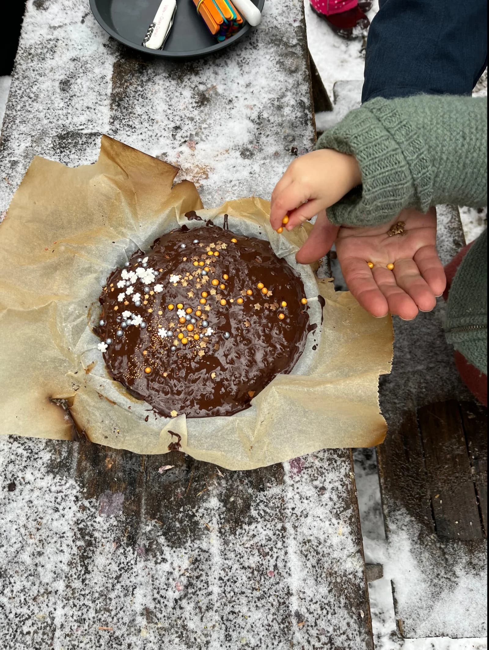 Kinderhand dekoriert einen Schokoladenkuchen an einem verschneiten Waldtisch